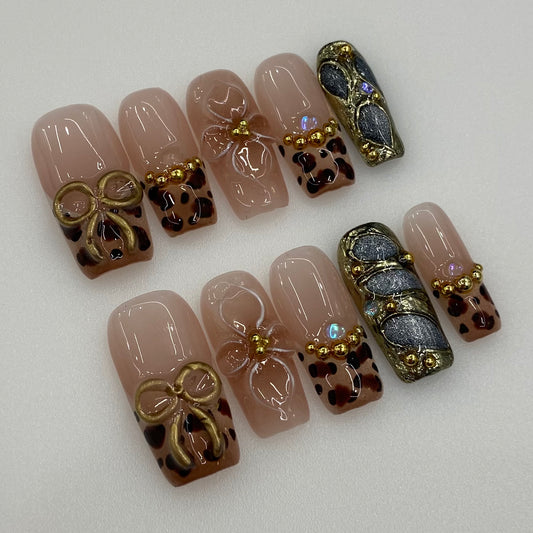 Flat lay photo of Golden Muse nails showing 3D gold bow and beaded French rims