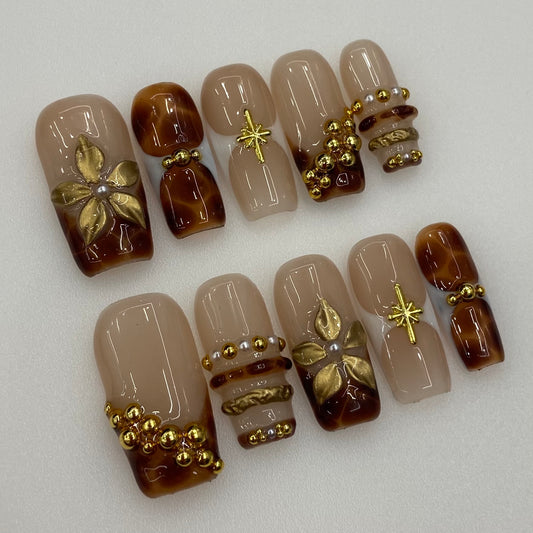 Flat lay photo of Mocha Muse nails showing 3D gold blossoms and beaded bangles