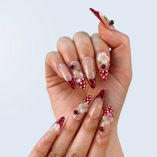 On-hand try-on of Whimsical Ladybug Garden nails showing 3D ladybugs and white petals