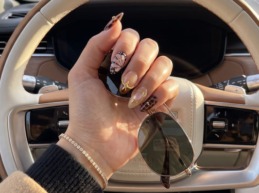 Handcrafted Gilded Tortoise almond tortoiseshell press-on nails captured from the driver's seat in afternoon sunlight, displaying translucent gel depth and gold charms