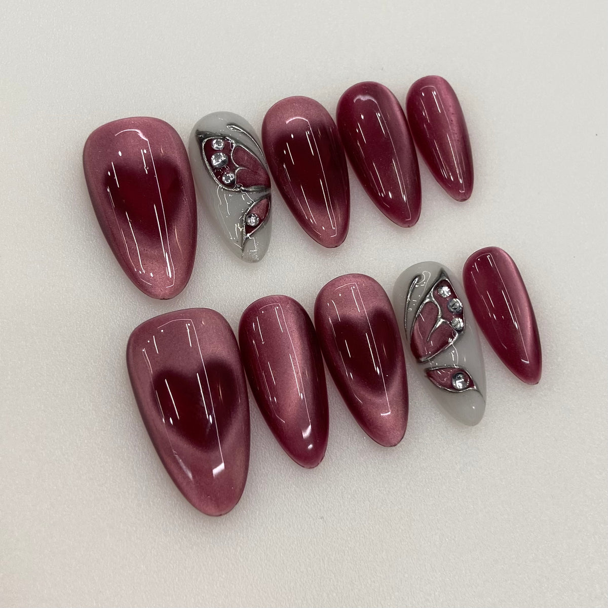 Flat lay photo of Burgundy Veil nails showing magnetic heart glow and butterfly art
