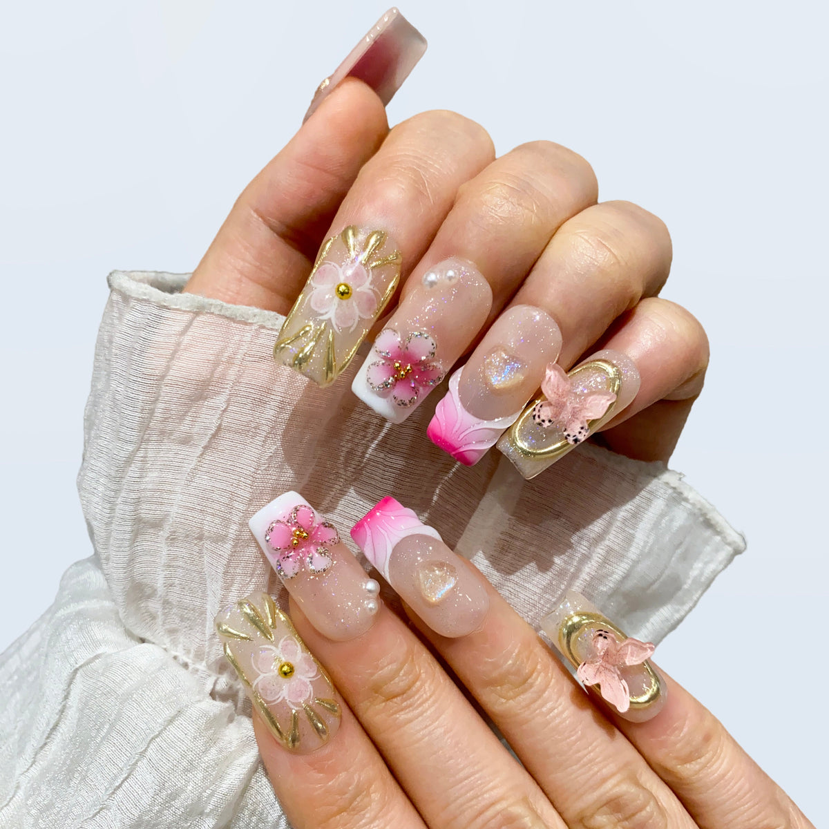 Both hands wearing Ribbon Dream coquette floral square nails on white sleeve