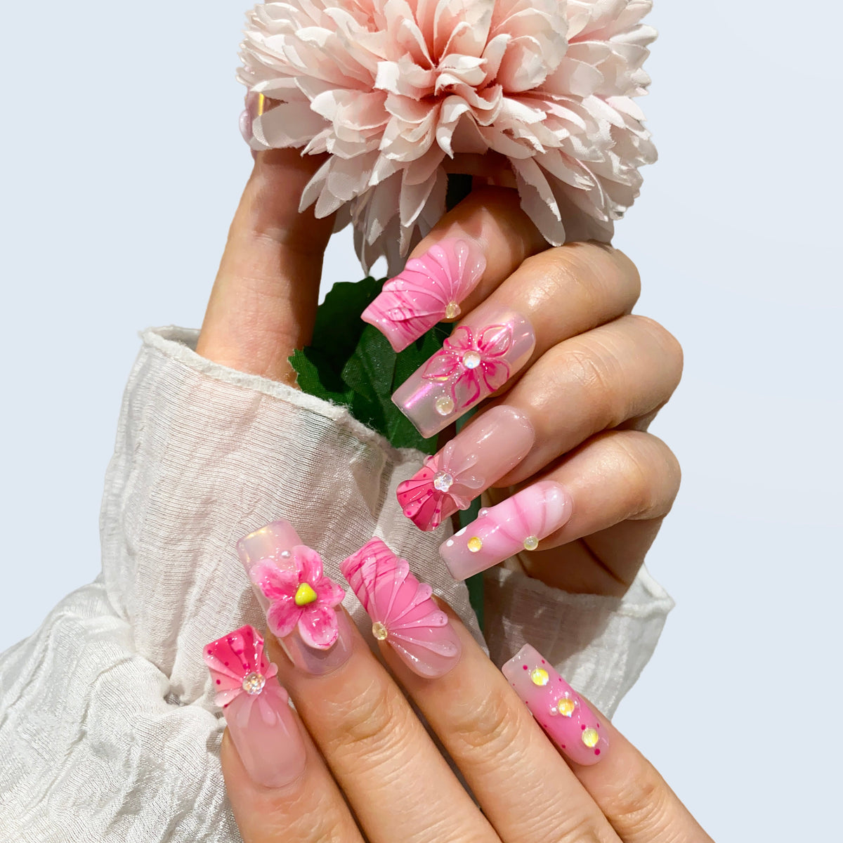 Hand display of Blush Bloom Spark square nails holding a pink flower prop