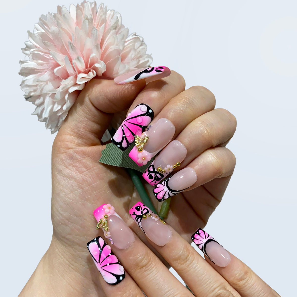 Hand wearing Sugar Noir Butterfly square nails holding a pink flower