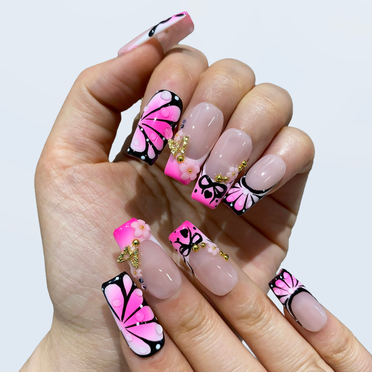 Close-up on-hand photo of Sugar Noir Butterfly nails featuring pink winged accent nails