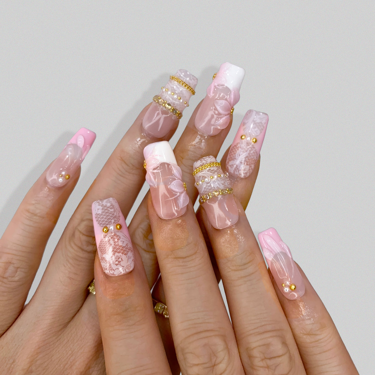 Angled view of Blush Lace press-on nails displaying pink French tips and gold accents