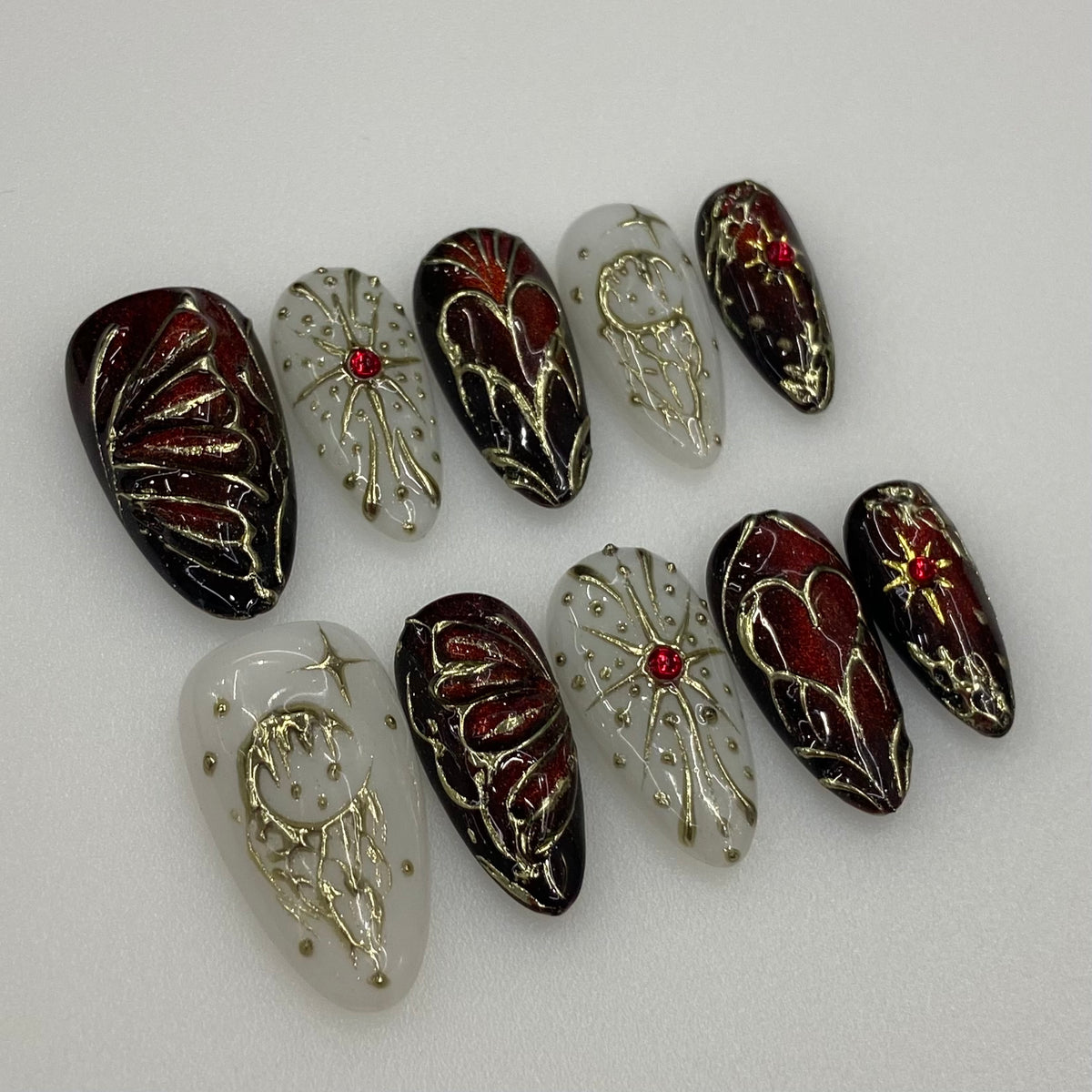 Full set photo of Crimson Alchemy gothic almond press-on nails displaying blood red and milky white contrast with golden alchemy art