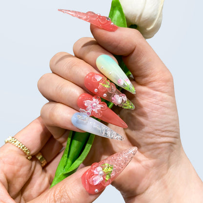 Both hands wearing Blush Bloom pastel floral press-on nails holding a flower