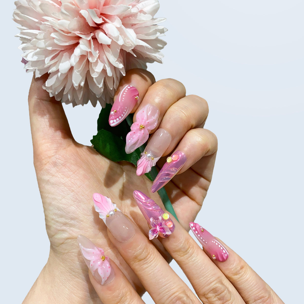 Hand display of Butterfly Kisses almond nails holding a flower prop in bright light