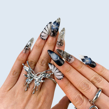 On-hand try-on of Noir Elegance stiletto nails showing gothic floral and silver accents