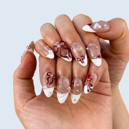 Both hands wearing Ribbon Bliss coquette French press-on nails in soft light