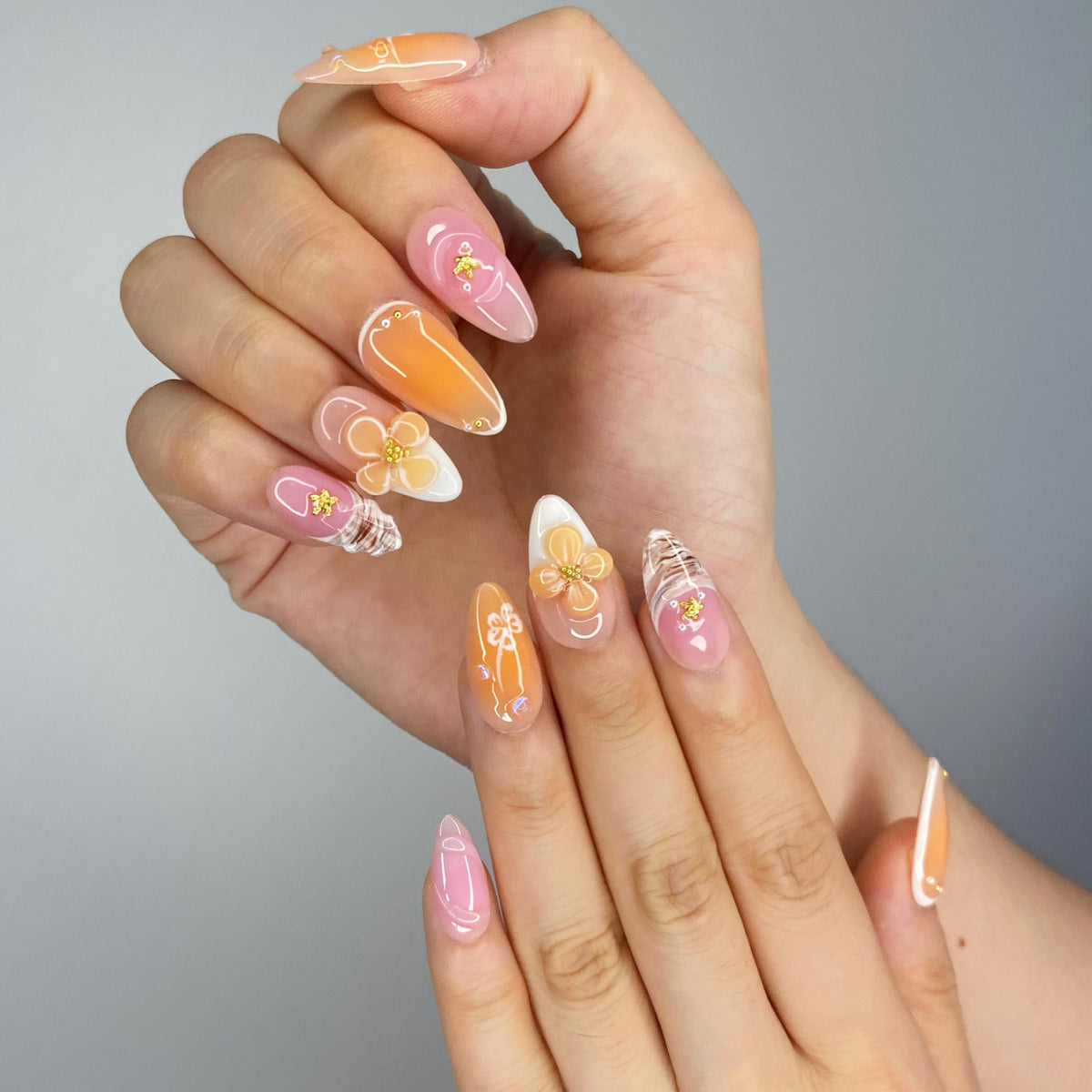 On-hand try-on of Orange Blossom nails showing sunlit peach gradient and 3D flowers