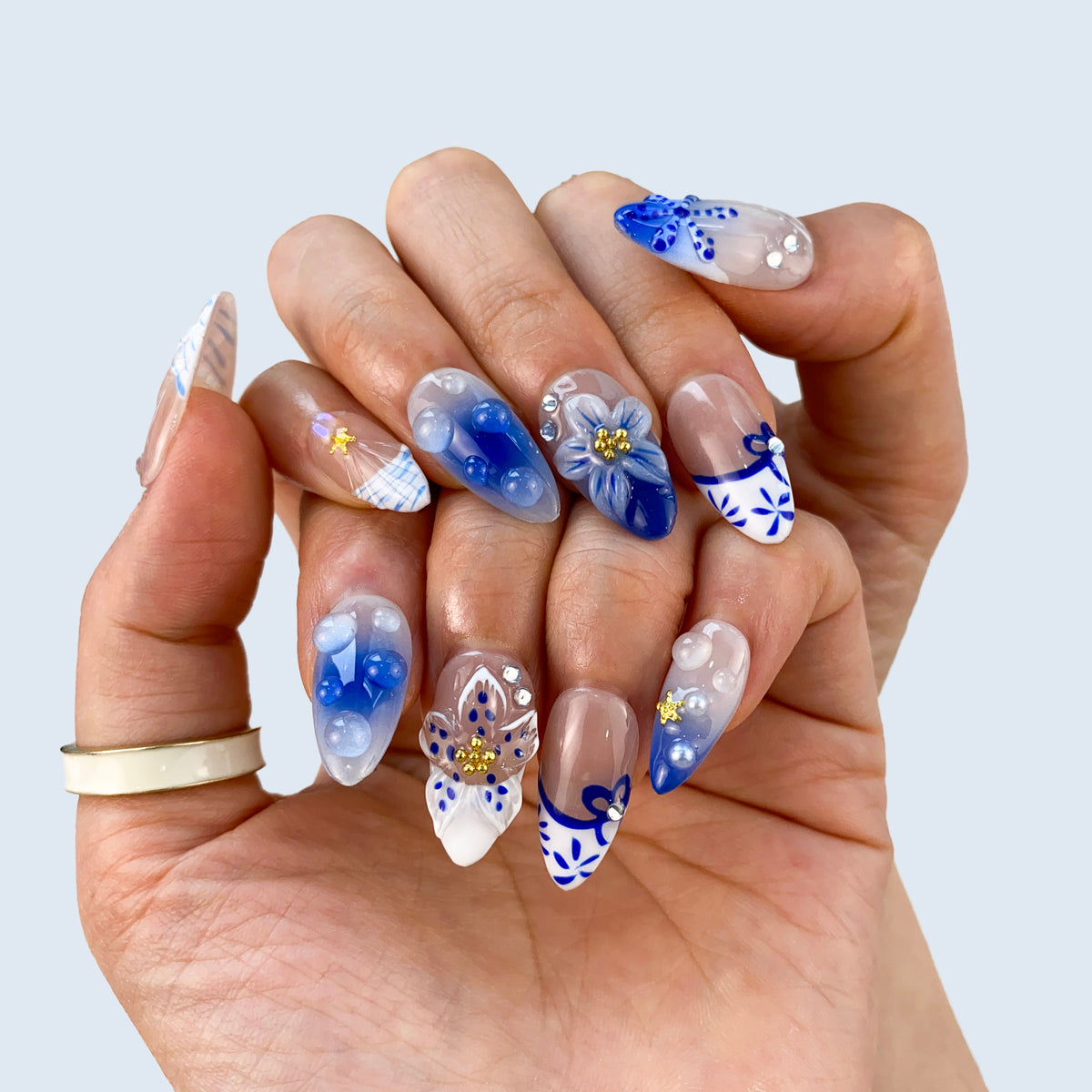 Angled view of Oceanic Mirage nails displaying 3D blue petals and gold star charms