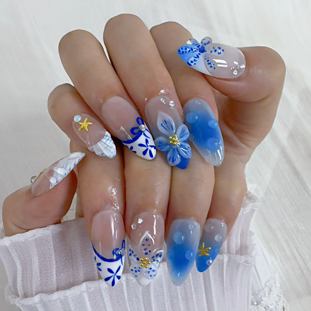 Single hand wearing Oceanic Mirage blue gradient almond press-on nails on sleeve