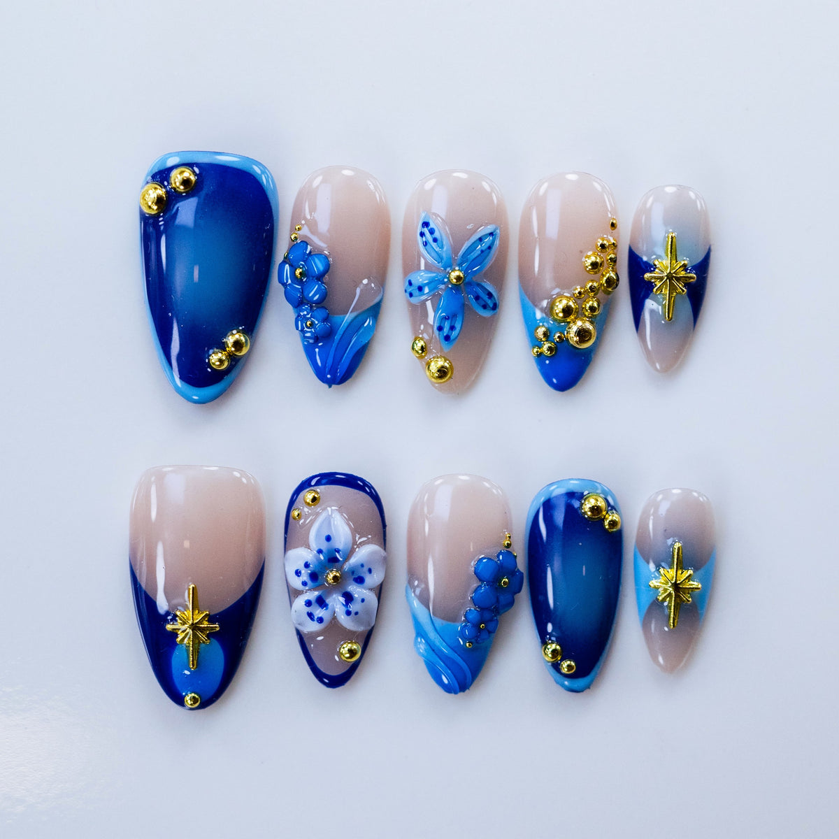 Flat lay display of Moonlit Petals nails showing 3D blue floral charms and gold beads