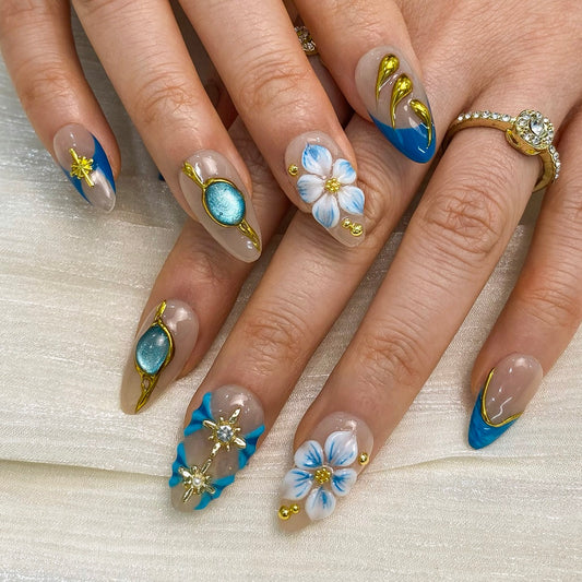 On-hand try-on of Celestial Shore almond nails showing blue French and gold drops