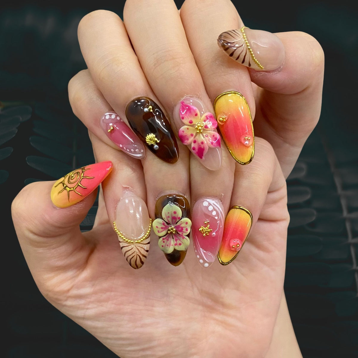 On-hand try-on of Sunset Bloom nails displaying warm amber tortoiseshell and flowers