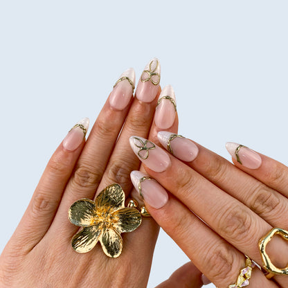 Both hands wearing Gilded Pearl Bow French press-on nails styled with gold rings