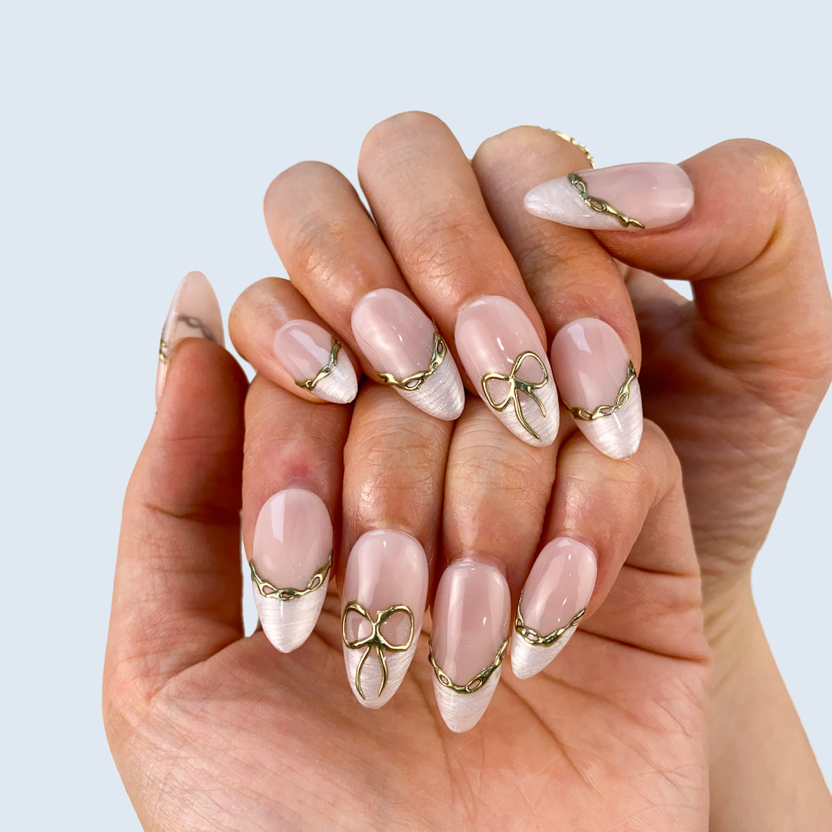On-hand try-on of Gilded Pearl Bow nails showing molten gold wire French borders