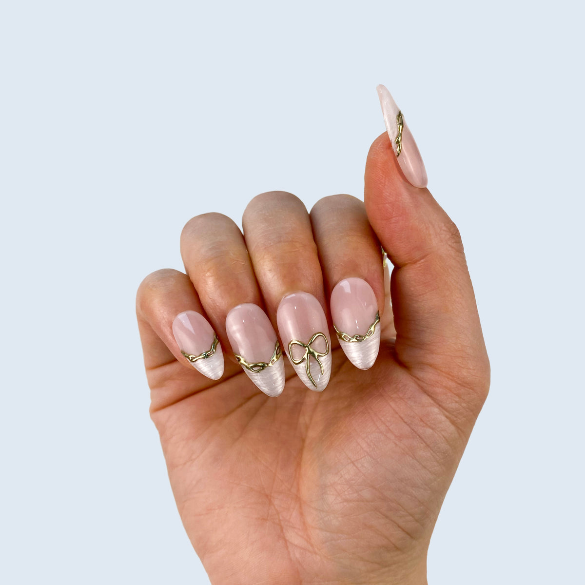 Single hand wearing Gilded Pearl Bow sheer nude and gold outline French nails