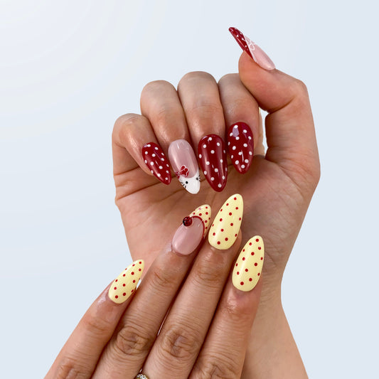 On-hand try-on of Cherry Drizzle nails showing contrasting red and yellow polka dots